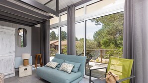 A modern living room with a sofa, a chair, a small table, and a window with a view of trees. - Villa with Stunning Views, Terrace and Garden (Moliets-et-Maa)