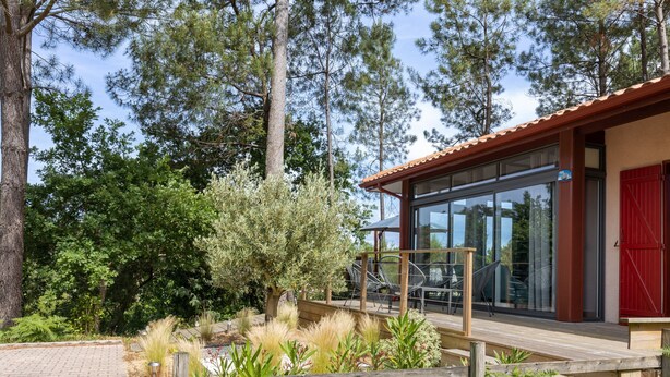 A modern building with a wooden deck, glass doors, and a red door. - Villa with Stunning Views, Terrace and Garden (Moliets-et-Maa)