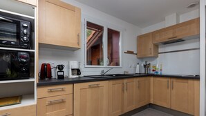 A modern kitchen with wooden cabinets, a black countertop, and a window with a view. - Villa with Stunning Views, Terrace and Garden (Moliets-et-Maa)