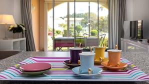 A dining area with a table set with colorful cups and saucers, a lamp, and a view of the outdoors. - T3 with Heated Pool, Private Garden, and Golf Nearby – Moliets (Moliets-et-Maa)