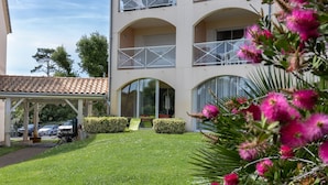 A multi-story building with balconies, a covered parking area, and a well-maintained lawn. - T3 with Heated Pool, Private Garden, and Golf Nearby – Moliets (Moliets-et-Maa)