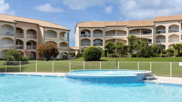 A swimming pool with a hot tub, surrounded by a fence, and a building with balconies and arched windows. - T3 with Heated Pool, Private Garden, and Golf Nearby – Moliets (Moliets-et-Maa)