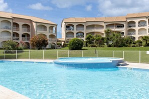 A swimming pool with a hot tub, surrounded by a fence, and a building with balconies and arched windows. - T3 with Heated Pool, Private Garden, and Golf Nearby – Moliets (Moliets-et-Maa)