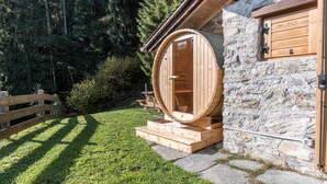 Een houten sauna met een stenen muur, een houten deur en een houten bank.