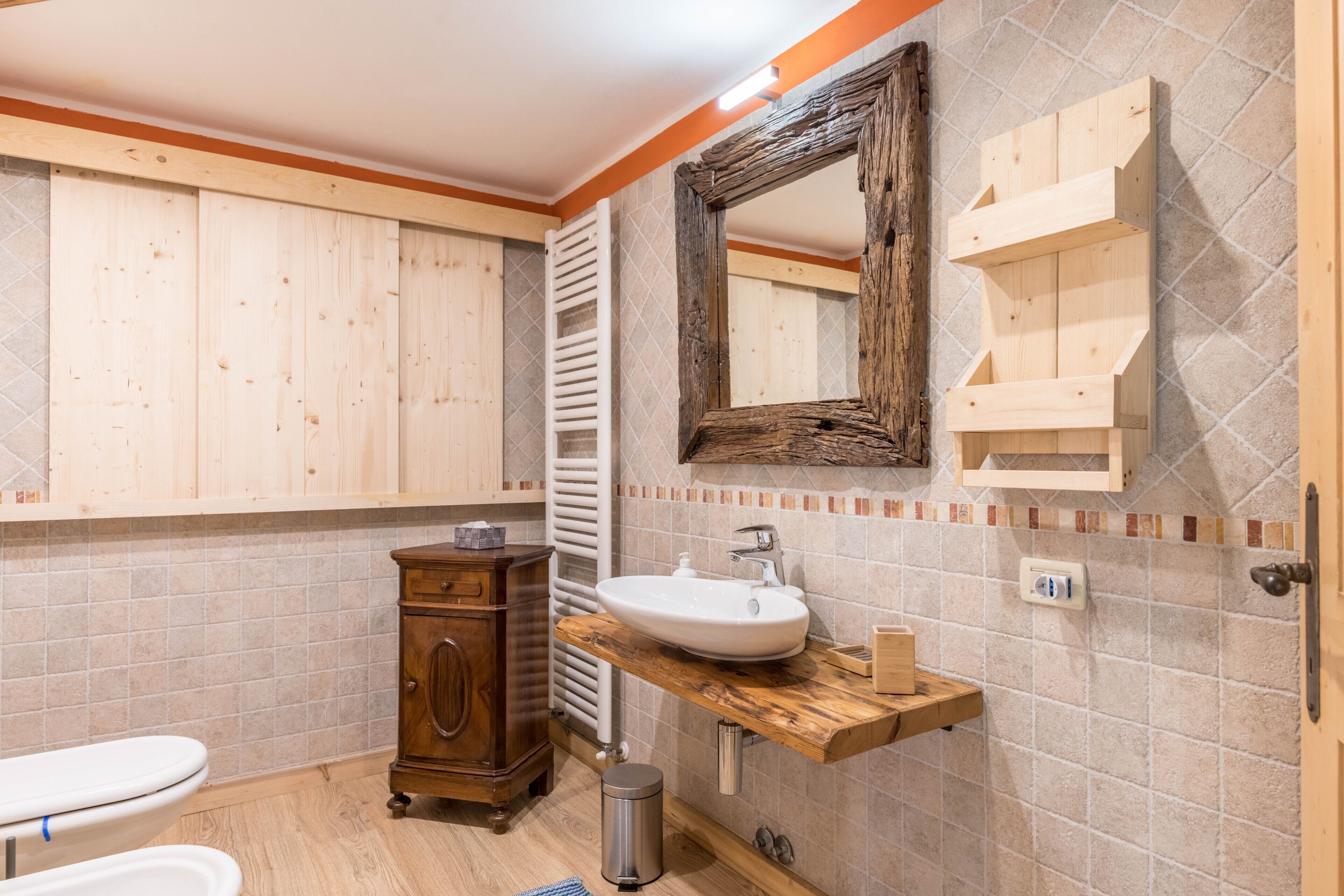 Ein Badezimmer mit einem Holzbadezimmerhocker, einem Waschbecken, einem Spiegel und einer Toilette.