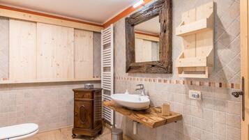 Ein Badezimmer mit einem Holzbadezimmerhocker, einem Waschbecken, einem Spiegel und einer Toilette.