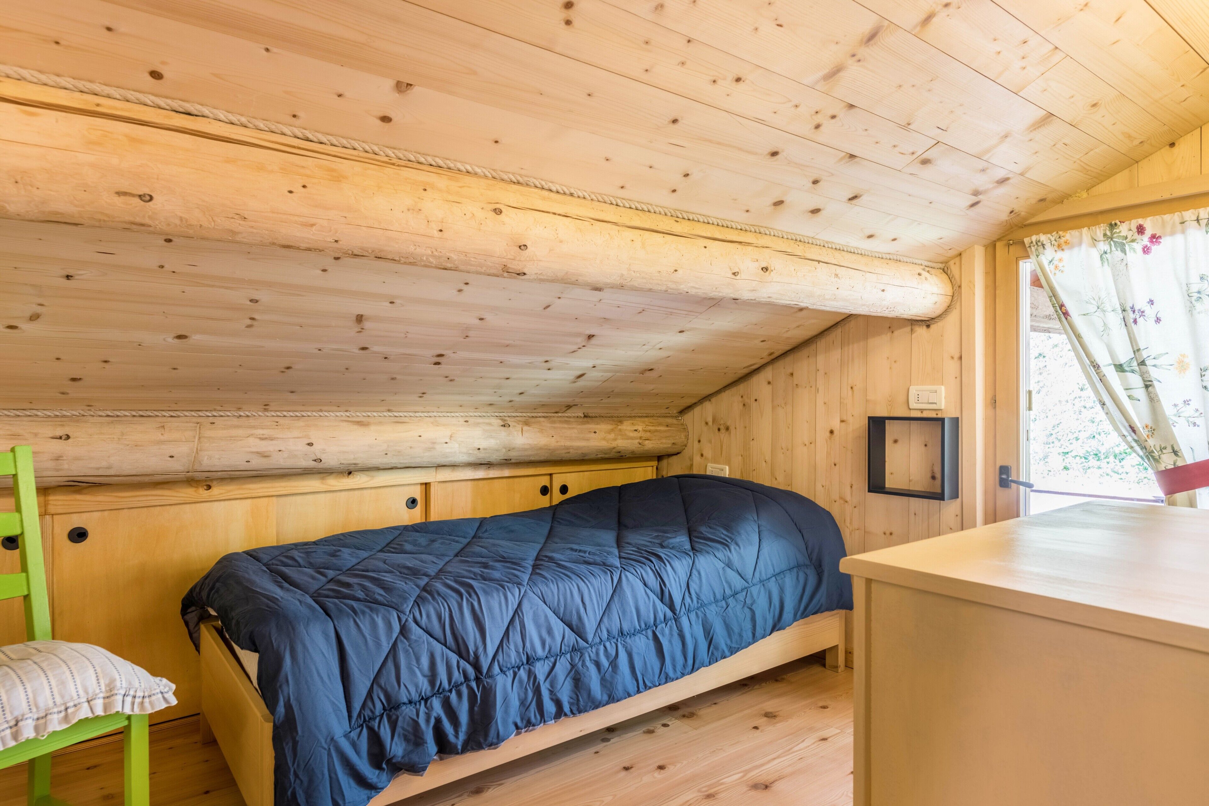 Ein Zimmer in einer Holzhütte mit einem Etagenbett, einem kleinen Schreibtisch und einem Fenster mit blumigen Vorhängen.