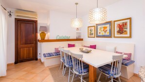 Un espace repas avec une table blanche, des chaises à rayures bleues, un banc en bois et une enseigne indiquant « Cuisine ».
