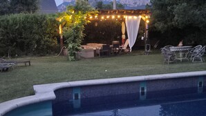 A backyard with a pool, a pergola with string lights, a table with chairs, and a small table with a vase. - Yoar Holiday Home with Mountain Views and Wi-Fi (Sant Llorenc de Morunys)