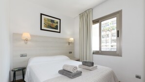 Hotellihuone, jossa on suuri sänky, kaksi seinälle asennettua lamppua, kehystetty taulu ja ikkuna, jossa on verhot.