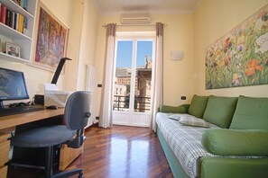 Une pièce comprenant un bureau, une chaise, un canapé vert et une vue sur l’extérieur, visible à travers une porte.