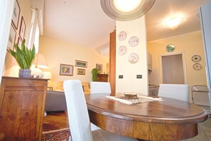 Un coin repas avec une table en bois, des chaises blanches, une plante en pot et des horloges fixées au mur.