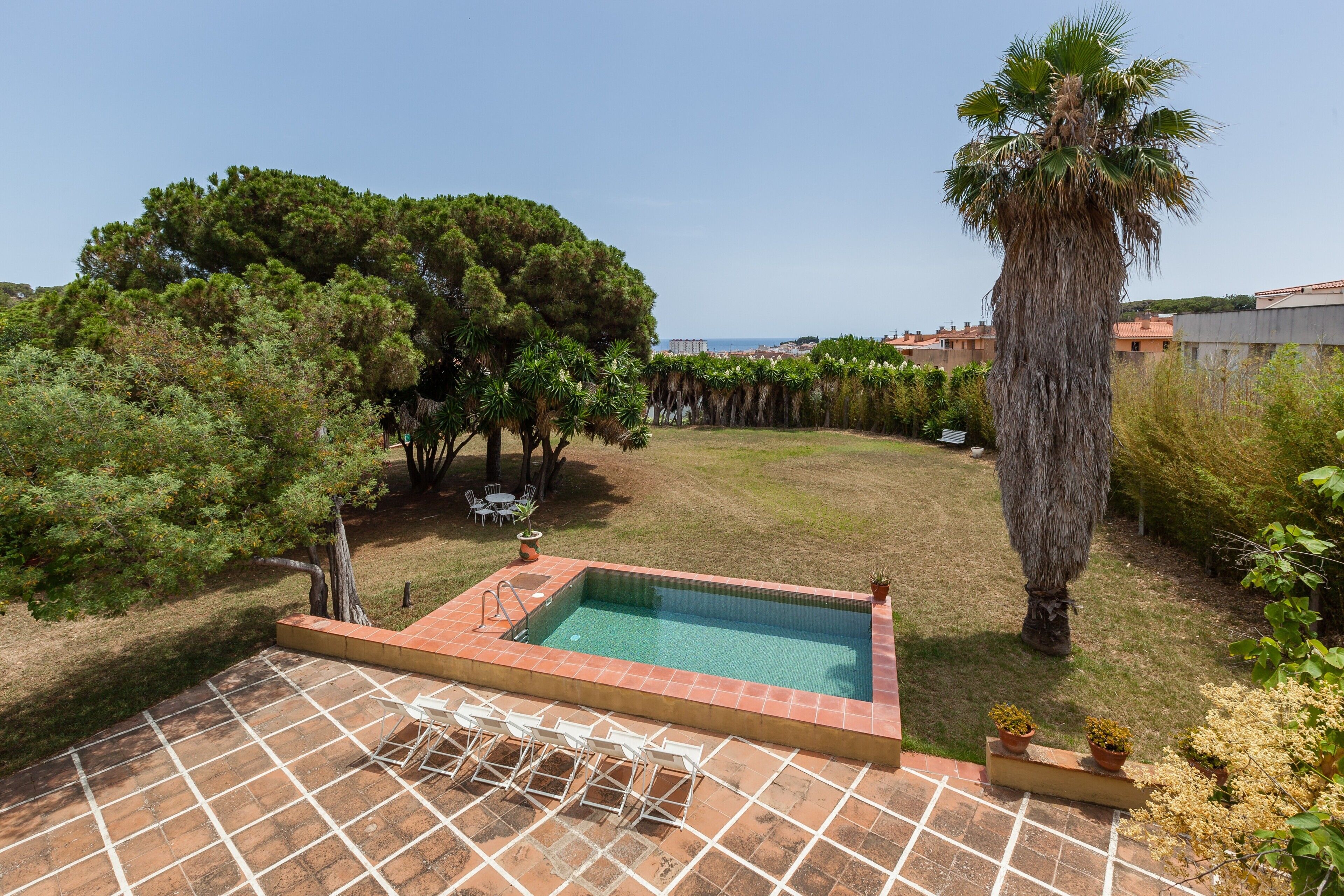 Piscina con borde de baldosas, rodeada de árboles y vistas a edificios.