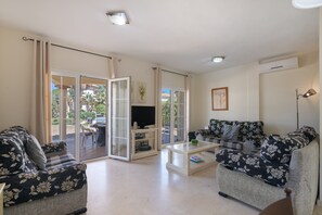 Un salón con dos sofás, una mesa de centro, un televisor y un ventanal corredero que da a un espacio exterior.