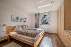 Une chambre à coucher avec un lit en bois, une table de chevet, une fenêtre donnant sur un beau paysage et une œuvre d’art accrochée au mur.