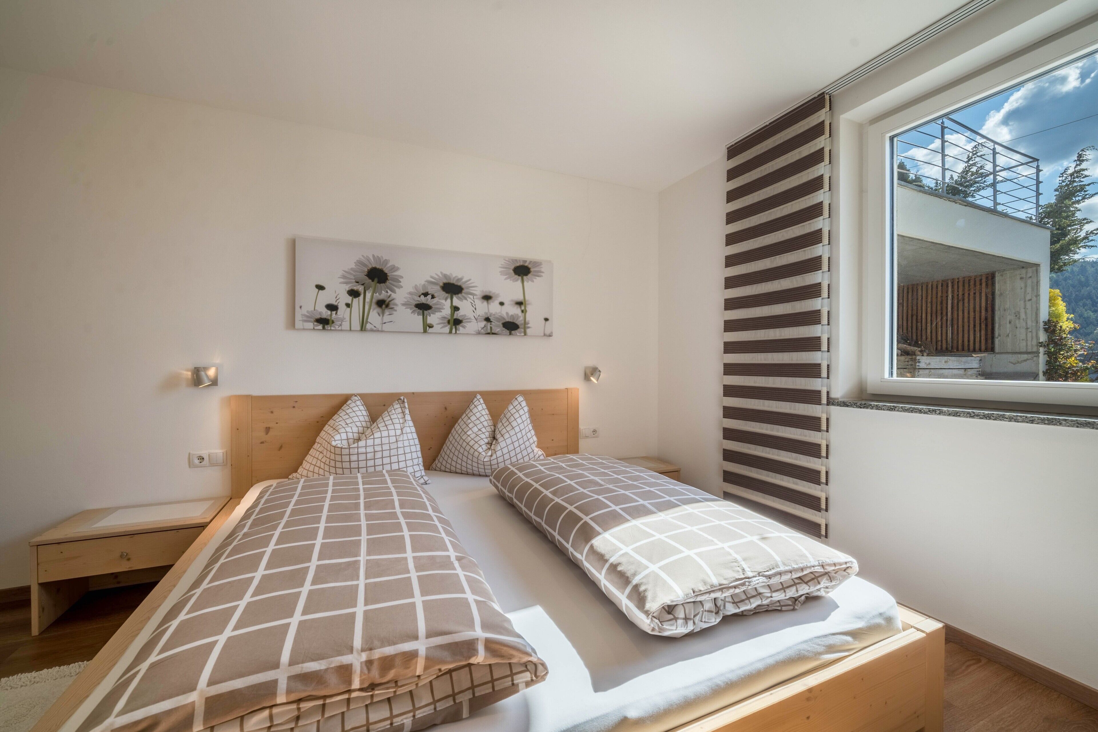 A bedroom with two beds, a nightstand, a wall-mounted artwork, and a window with a view.