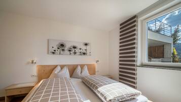A bedroom with two beds, a nightstand, a wall-mounted artwork, and a window with a view.