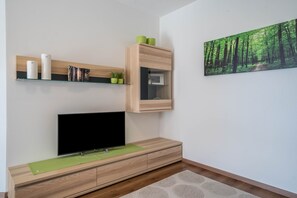 A modern living room with a flat-screen TV, wooden shelving, a framed picture, and a green rug.