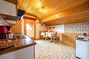 A kitchen with wooden ceiling, a dining table with chairs, a refrigerator, and a sink.