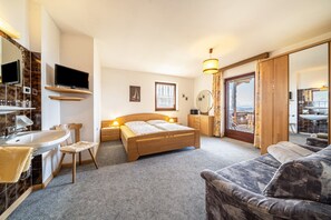 Ein Schlafzimmer mit Bett, Nachttisch, Lampe, Fernseher und Blick durch ein Fenster.