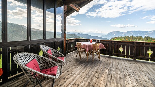Eine Holzterrasse mit Korbstühlen und einem Tisch, mit Blick auf eine gebirgige Landschaft.