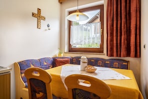 A dining area with a table, chairs, a cross on the wall, and a window with curtains.