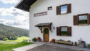 Ein Gebäude mit einem Schild, das 'Bottleiner Hof' zeigt, Steinstufen, die zu einer Holztür führen, und Blumentöpfen im Erdgeschoss.
