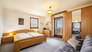 Ein Schlafzimmer mit Bett, Nachttischen, einem Schminktisch, einem Spiegel, einem Fenster mit Vorhängen, Blick auf einen Balkon und einem Sofa.