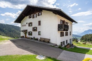 A two-story building with a sloped roof, a balcony on the upper floor, and a bench outside.