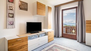 Une chambre moderne dotée d’une télévision, d’armoires en bois, d’un balcon avec des rideaux et d’une œuvre d’art murale inspirante.