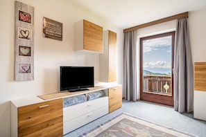 Une chambre moderne dotée d’une télévision, d’armoires en bois, d’un balcon avec des rideaux et d’une œuvre d’art murale inspirante.