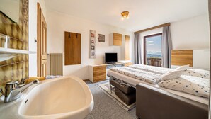 Une chambre d’hôtel moderne dotée d’une grande baignoire, d’un lit avec vue, d’un bureau avec un téléviseur à écran plat et d’une armoire en bois.