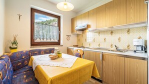 Une cuisine compacte avec des meubles en bois, un coin repas doté d’une table jaune et une fenêtre donnant sur des arbres.