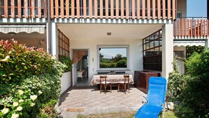 Un espacio al aire libre techado con una mesa y sillas, una silla reclinable azul y vistas a zonas verdes.