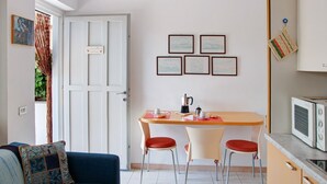 Un espacio habitable compacto con kitchenette, un comedor con dos sillas y un sofá con un cojín estampado.