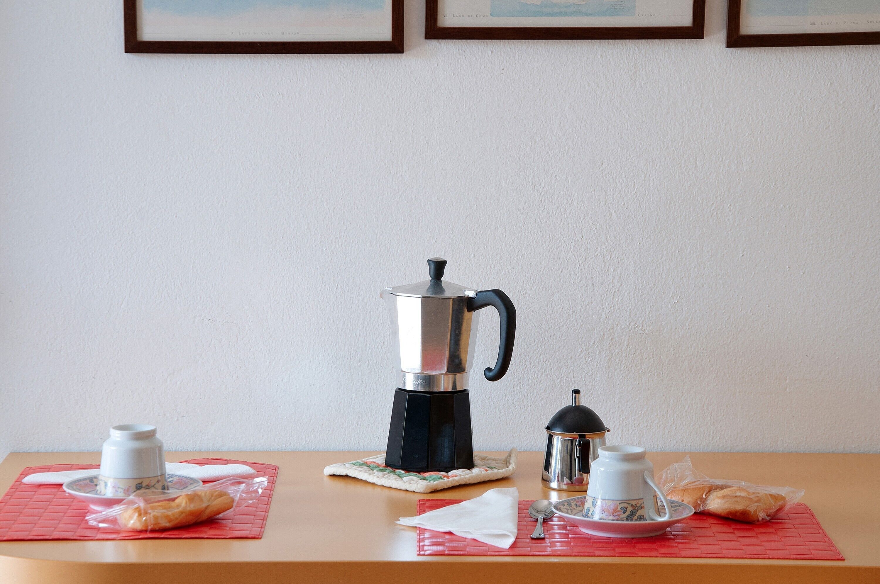 Een ontbijt met een koffiezetapparaat, kopjes en gebak op een tafel.
