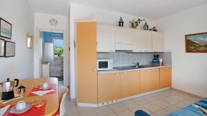 Una cocina compacta con microondas, pileta y alacenas, un comedor con mesa y sillas, y vista al exterior.