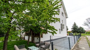 Un edificio residencial con un patio cercado, mobiliario exterior y un árbol que da sombra.