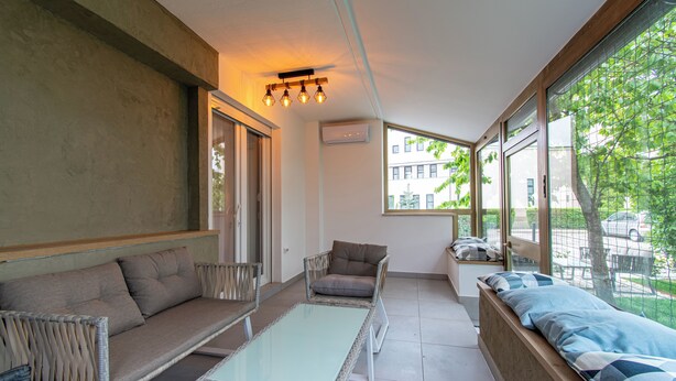 Una habitación moderna con sofá, sillón, una mesa de vidrio y ventanas amplias que ofrecen vistas al exterior.
