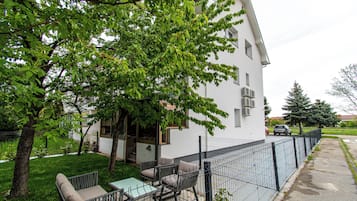 A residential building with a fenced patio area, outdoor seating, and a tree providing shade.