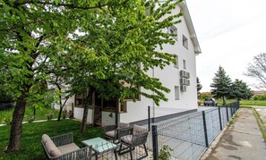 Ein Wohngebäude mit umzäunter Terrasse, Sitzgelegenheiten im Freien und einem Baum, der Schatten spendet.