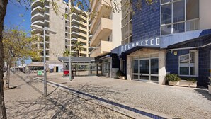 Un edificio moderno con un letrero que dice 'ATLANTICO', un sendero pavimentado y una calle bordeada de árboles.