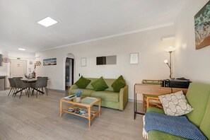 A living room with a green sofa, a wooden coffee table, and a dining area with chairs. - Apartment "Praia da Rocha" with Sea View, Balcony & Wi-Fi (Portimão)