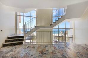 A spacious interior with a marble staircase, large windows, and a view of the sea. - Apartment "Praia da Rocha" with Sea View, Balcony & Wi-Fi (Portimão)