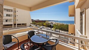 Un balcón con una mesa redonda y sillas, con vista a una playa y edificios.