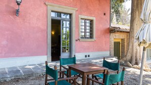 Un bâtiment rose avec une table et des chaises en bois, une fenêtre et une porte.