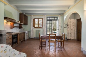A kitchen with wooden cabinets, a dining table with chairs, a window with curtains, and a radiator.