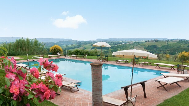 Une piscine entourée de verdure et de collines, avec des chaises longues et des parasols.
