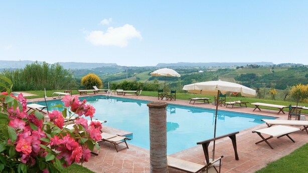 A swimming pool with lounge chairs and umbrellas, surrounded by greenery and a view of rolling hills. - Villa 'Villa del Fattore' with Shared Pool, Private Terrace & Wi-Fi (Montespertoli)