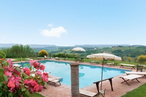 A swimming pool with lounge chairs and umbrellas, surrounded by greenery and a view of rolling hills. - Villa 'Villa del Fattore' with Shared Pool, Private Terrace & Wi-Fi (Montespertoli)